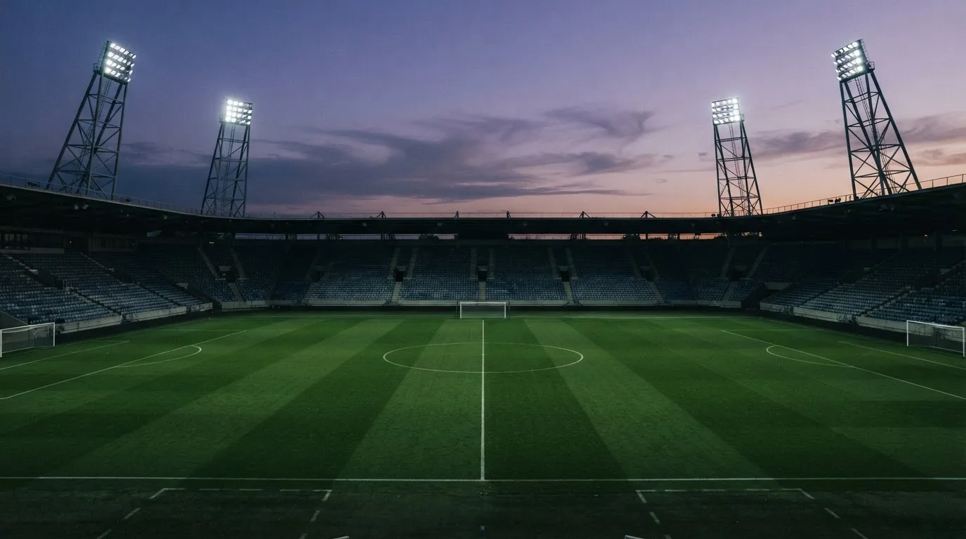 Een leeg voetbalstadion met lichtmasten bij schemering