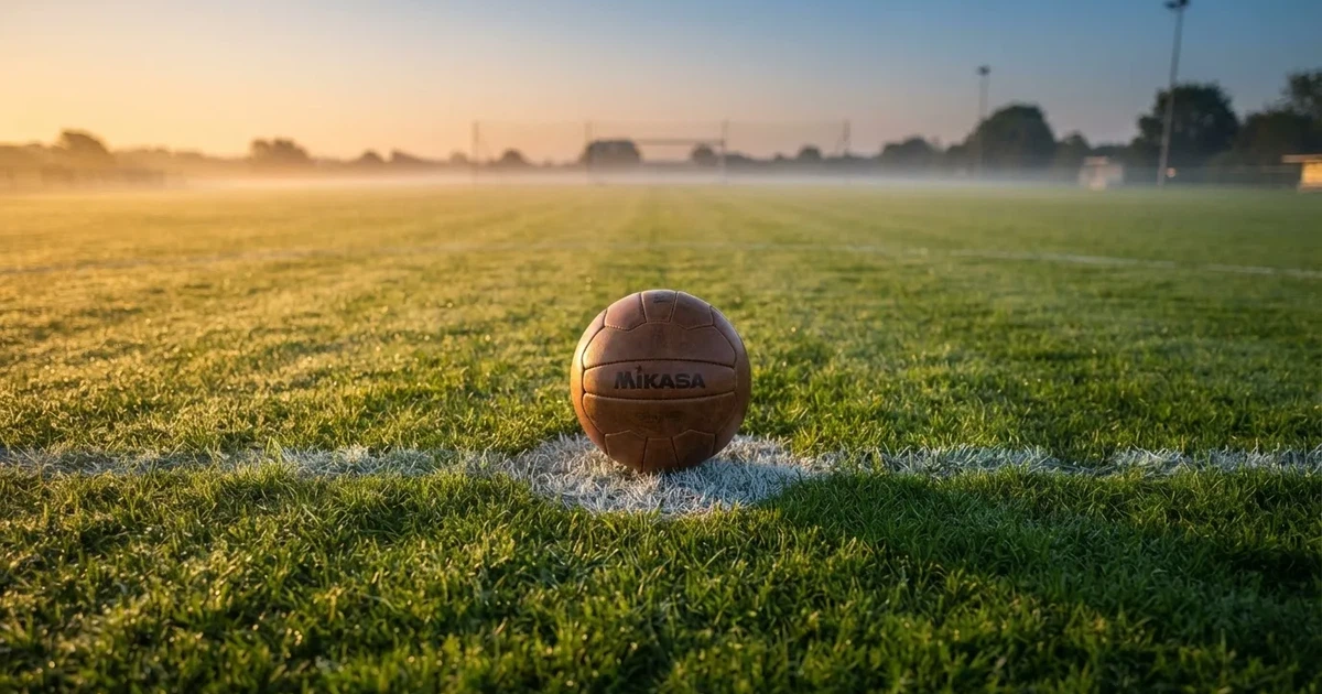 Een voetbal op de middenstip van een grasveld in het ochtendlicht
