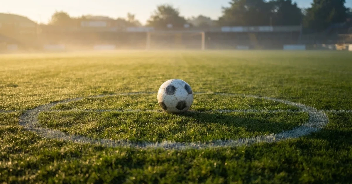 Een voetbal op de middenstip van een grasveld in het ochtendlicht