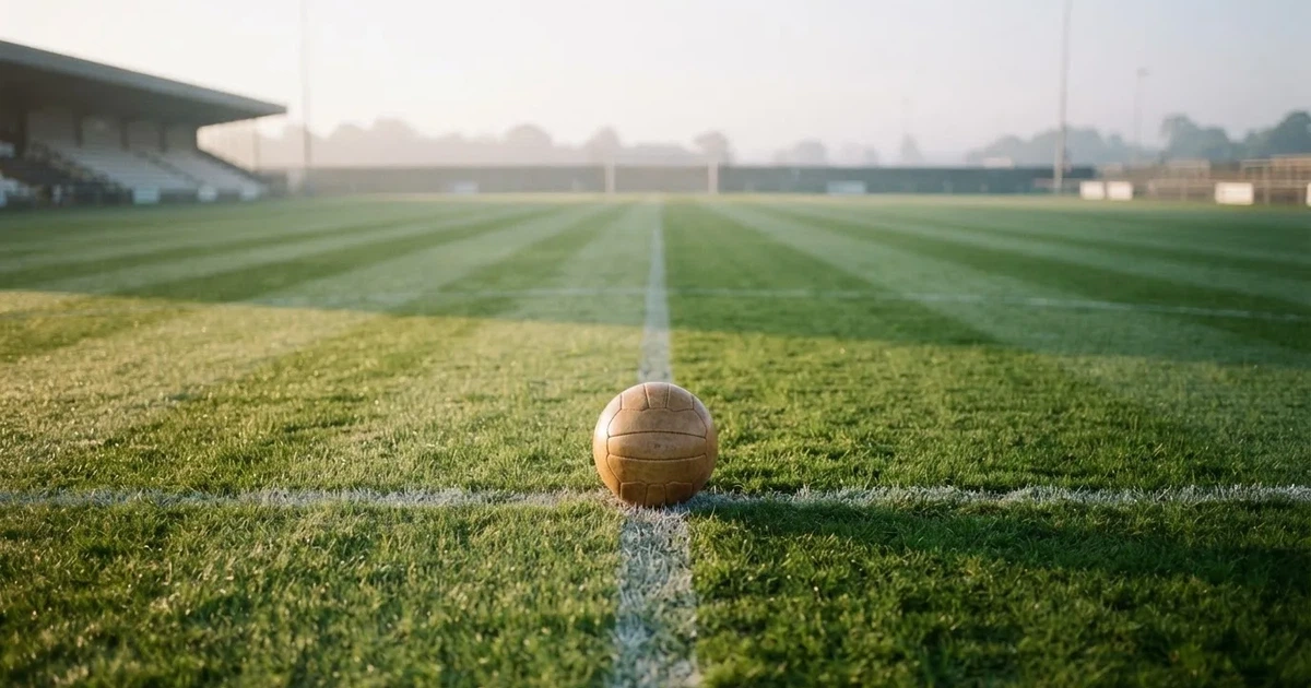 Een voetbal op de middenstip van een grasveld in het ochtendlicht