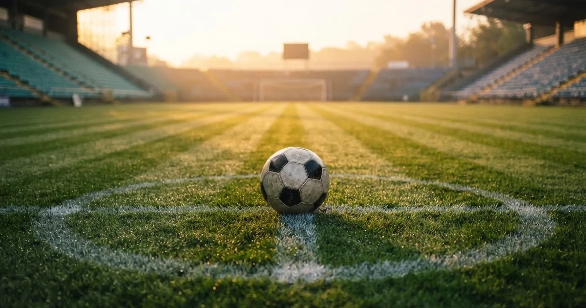 Een voetbal op de middenstip van een grasveld in het ochtendlicht